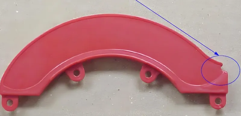 Red plastic stamped part with mounting holes and an arrow pointing to a defect