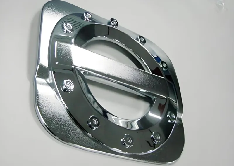 A close-up image of a chrome-plated fuel door with bolt detail