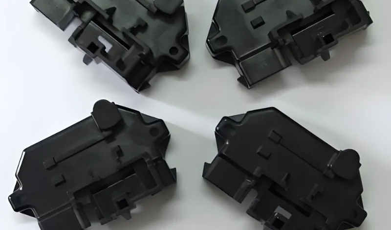 Top view of four identical black plastic components on a white background