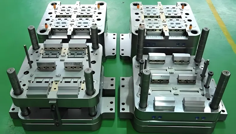 A set of industrial metal molds on a green factory floor, with various components and structures