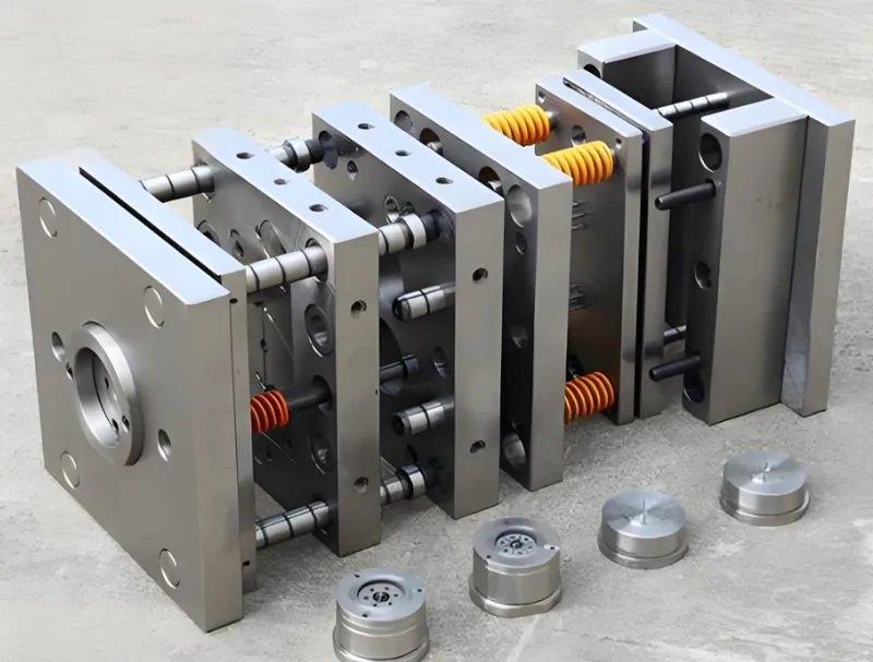 An image showing an exploded view of metal components used in an injection mold, with several plate sections and cylindrical parts