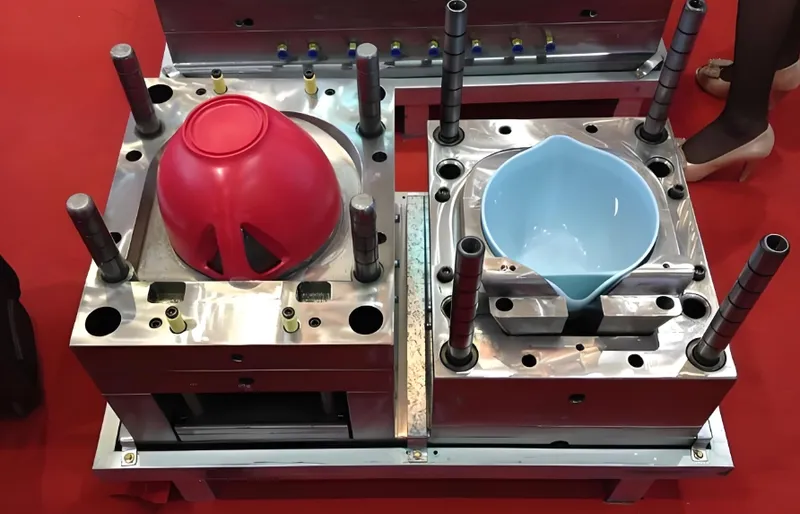 A machine for injection molding used to create plastic bowls, featuring a red and a blue bowl on a red floor