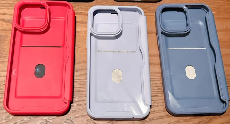 Three different colored iPhone 15 cases with lens covers placed on a wooden table
