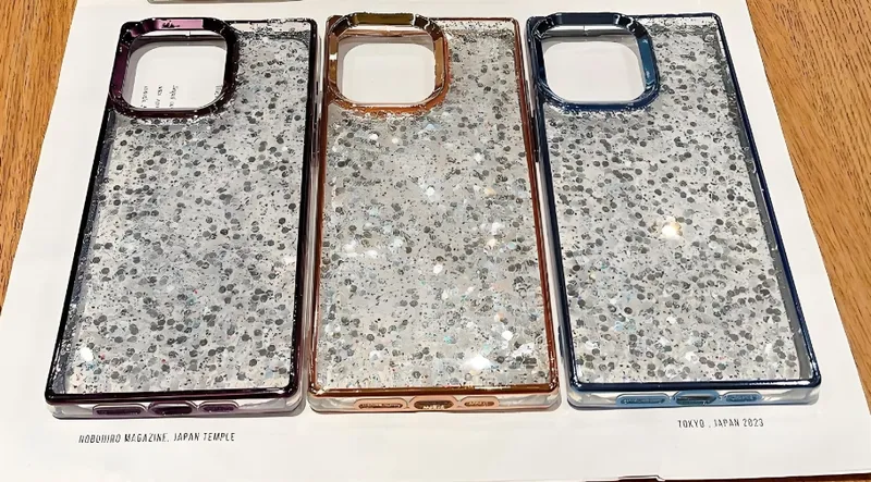 Three glittery phone cases with metallic frames in different colors on a table