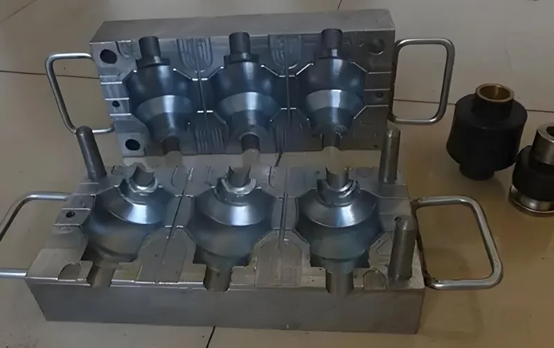 A metal mold with handles, showing hollow sections for casting, placed on a tiled floor