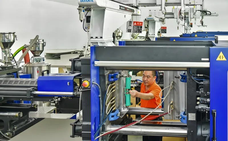 A worker operating a plastic injection molding machine in a factory setting