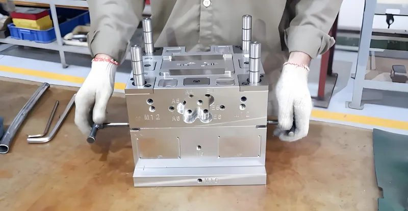A person wearing gloves handling a metal injection mold on a workbench