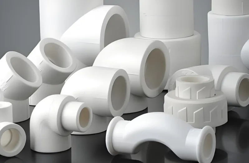 A variety of white PVC pipe fittings arranged on a dark surface