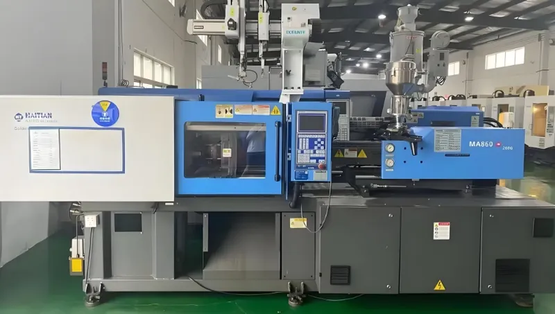 A large blue and white injection molding machine with technical controls and components, placed in an industrial setting.