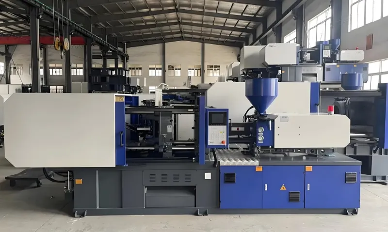 A blue and white industrial injection molding machine in a factory setting