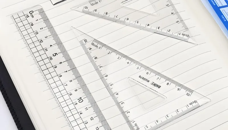A set of transparent triangular rulers placed on a lined notebook page