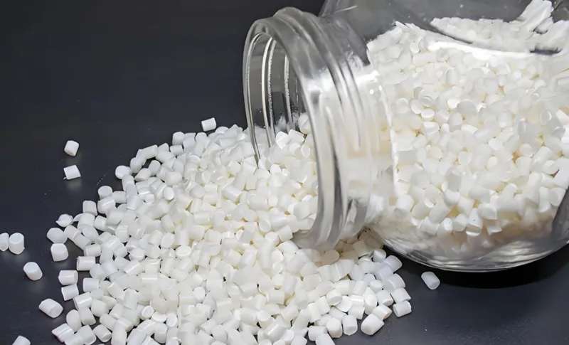 White plastic pellets spilling from a transparent jar onto a dark surface